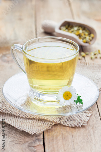 Chamomile tea in glass cup, chamomile flowers and dry tea on background, vertical