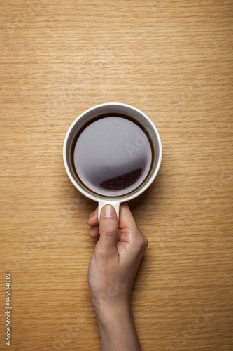 woman hand hold a cup of coffee on the wood background(desk, table)