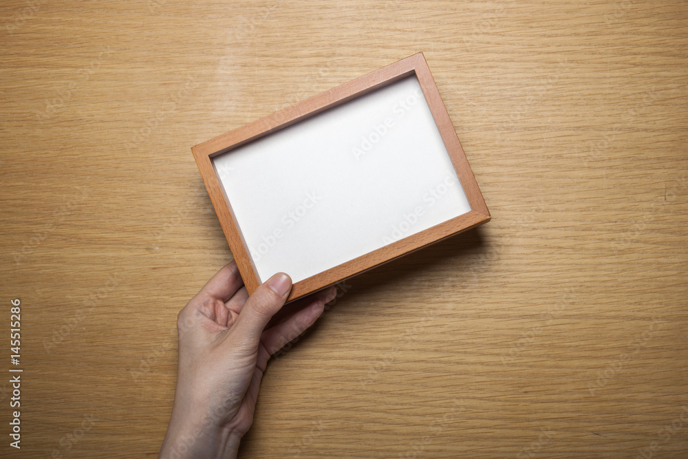 Fototapeta premium woman hand hold a photo frame on the wood table(background)
