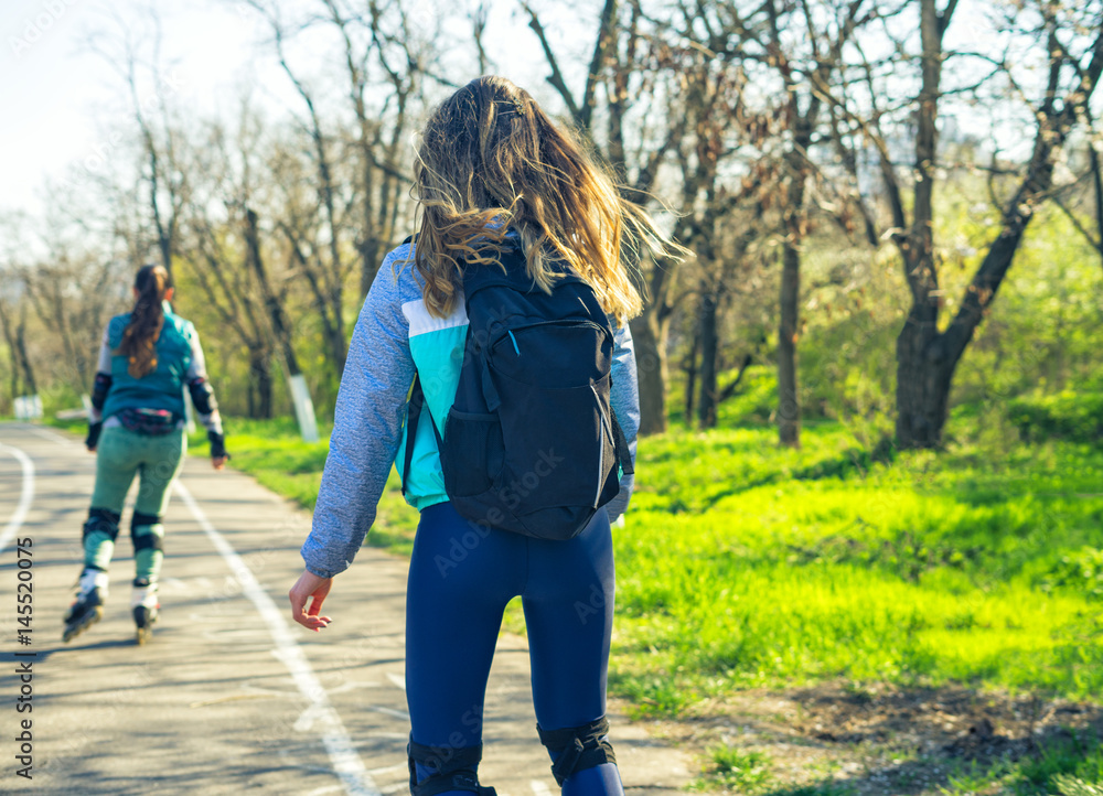 Two girls on roller skates ride along the road. Sport girls. One girl is ahead of the other. Second gitl is tired. Two girls on roller skates ride along the road. Sport girls. One girl is ahead of the other. Second gitl is tired.