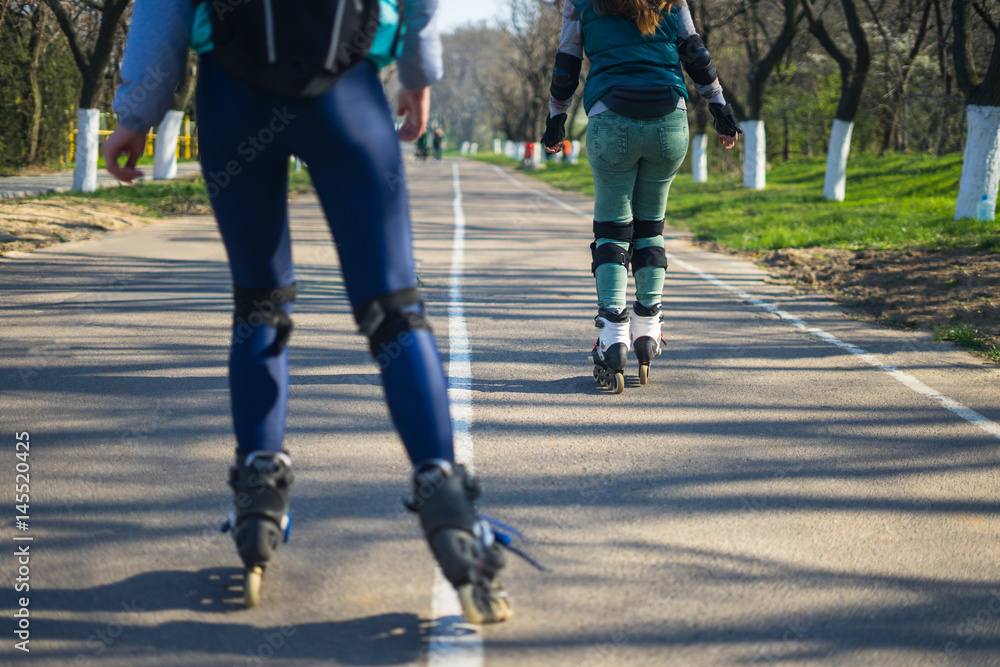 Competitions in roller skating.Two girls on roller skates ride along the road. The second girl is tired and stopping. Competitions in roller skating.Two girls on roller skates ride along the road. The second girl is tired and stopping.