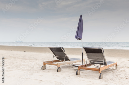 Fototapeta Naklejka Na Ścianę i Meble -  Beach chairs and umbrella on the white sand beach with cloudy sky, relaxation and vacation time.