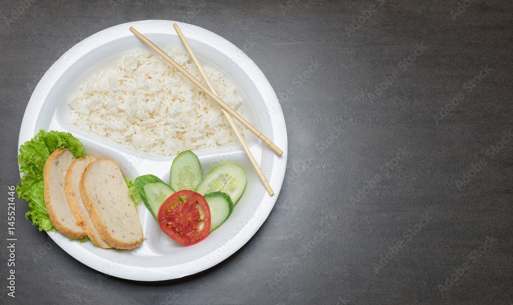 Disposable plastic food plate on black table. White plate with rice, meat and vegetables. Bamboo chopsticks. Healthy take-away concept. Place for copy space