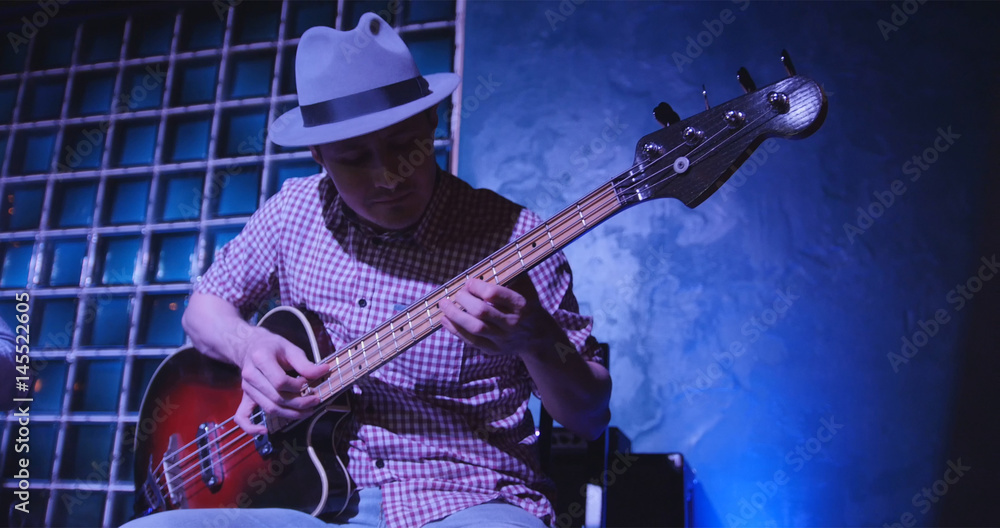 Fototapeta premium Guitarist at scene in bar - musician in hat plays guitar