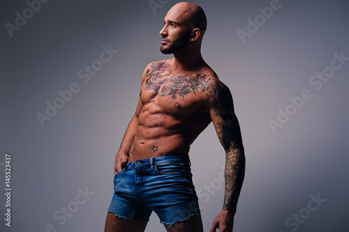 Obraz na plátne Shaved head, muscular male with tattoos on his torso over grey vignette background