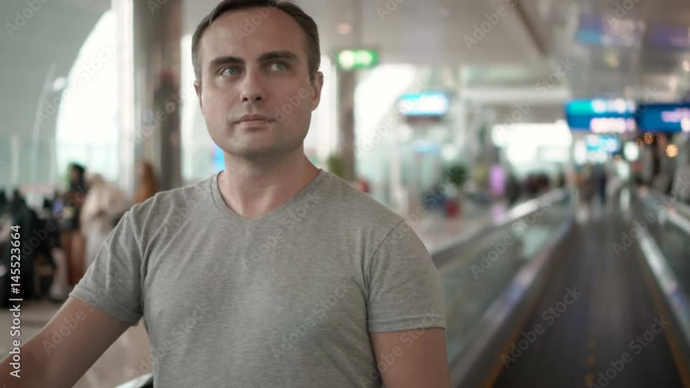 Handsome young man in airport terminal. Waiting for flight. Using travolator, looking around Handsome young man in airport terminal. Waiting for flight. Using travolator, looking around