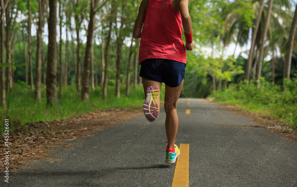 Young fitness woman running on morning tropical forest trail