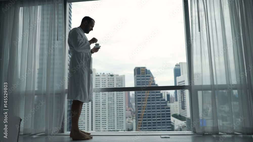 Young man in bathrobe drinking espresso standing by window at home
Young man in bathrobe drinking espresso standing by window at home