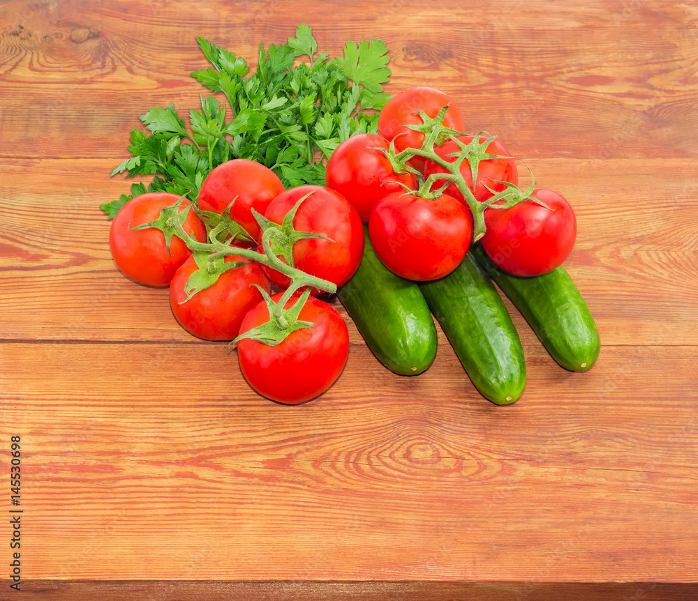 Cucumbers and branches of the red tomatoes on wooden surface