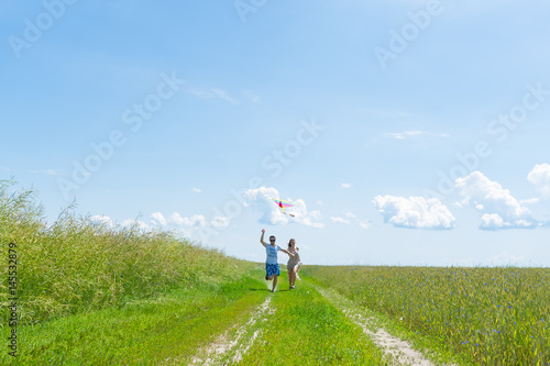 Lovely couple play air kite at green picturesque meadow at countryside