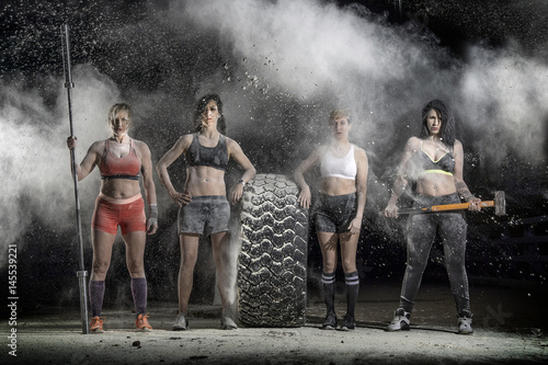 Portrait of women standing with a hammer and barbell posing with a tire in the dust photo