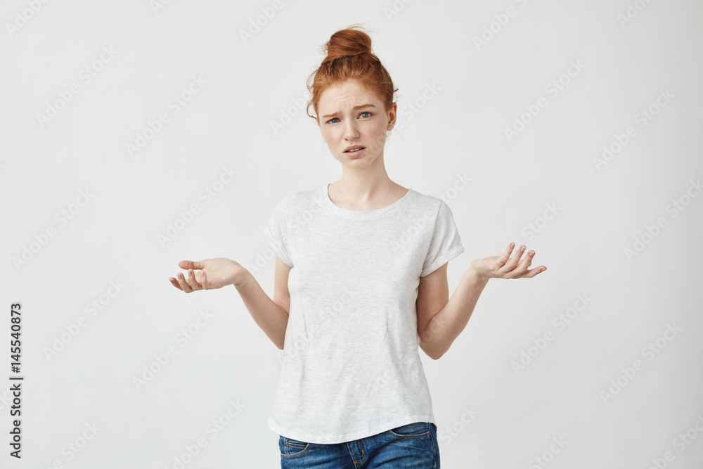 Young displeased redhead girl gesturing looking at camera. Confused girl arguing with a boyfriend. White background. Young displeased redhead girl gesturing looking at camera. Confused girl arguing with a boyfriend. White background.