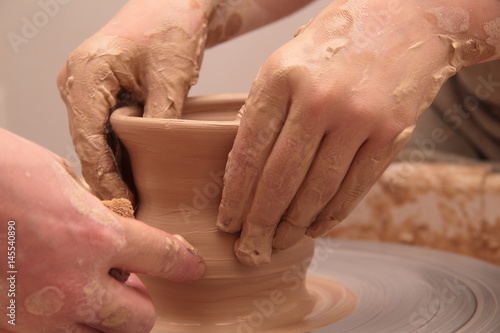 Hands of a potter, creating an earthen jar on pottery wheel. photo