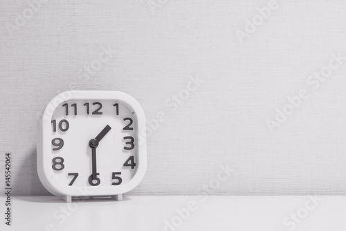 Closeup white clock for decorate show half past one o'clock or 1:30 p.m. on white wood desk and cream wallpaper textured background in black and white tone with copy space