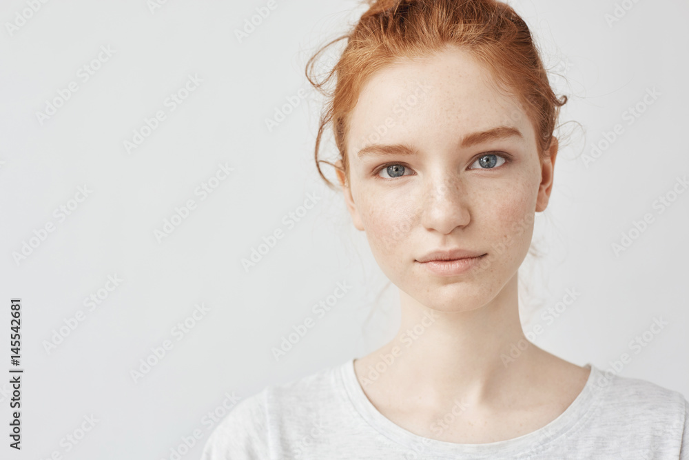 Fototapeta premium Close up portrait of young beautiful redhead girl in white shirt smiling looking at camera. Copy space. Isolated on white background.
