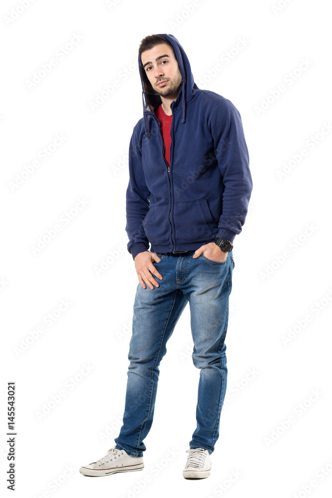 Charming man in blue hooded sweatshirt with hands in pockets looking at camera. Full body length portrait isolated over white studio background. Charming man in blue hooded sweatshirt with hands in pockets looking at camera. Full body length portrait isolated over white studio background.