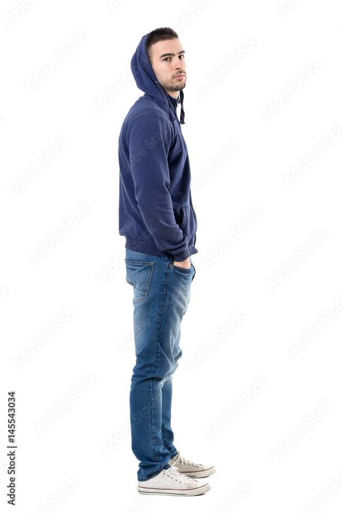 Profile of tough young casual man in blue hoodie looking intense at camera. Full body length portrait isolated over white studio background. Profile of tough young casual man in blue hoodie looking intense at camera. Full body length portrait isolated over white studio background.