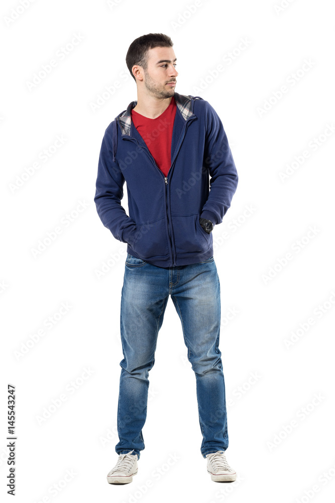 Fototapeta premium Cool young guy in blue sweatshirt with hands in pockets looking away. Full body length portrait isolated over white studio background.