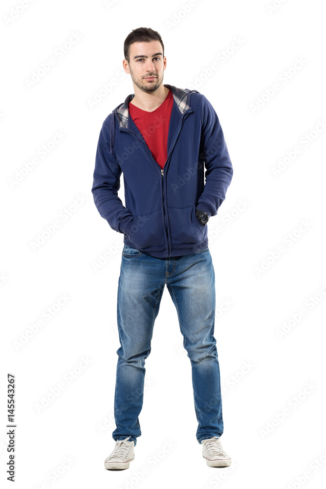 Charming young guy in blue sweatshirt with hands in pockets looking at camera. Full body length portrait isolated over white studio background. Charming young guy in blue sweatshirt with hands in pockets looking at camera. Full body length portrait isolated over white studio background.