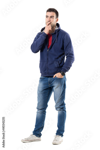 Pensive young casual guy with hand on chin looking up interested. Full body length portrait isolated over white studio background.
