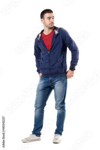 Relaxed young cool man in blue sweatshirt with hands in back pockets looking behind. Full body length portrait isolated over white studio background.