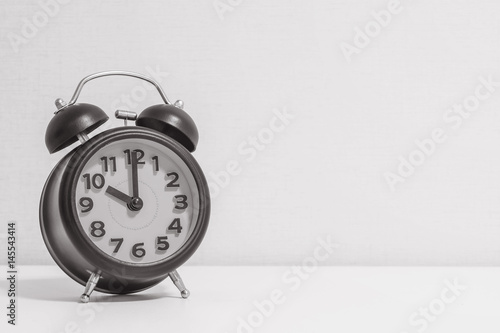 Closeup alarm clock for decorate in 10 o'clock on white wood desk and cream wallpaper textured background in black and white tone with copy space