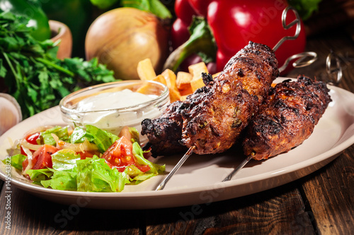 Grilled shish kebab served with fried chips and salad photo