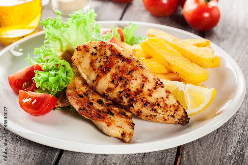 Grilled chicken breasts served with fries and fresh salad Grilled chicken breasts served with fries and fresh salad