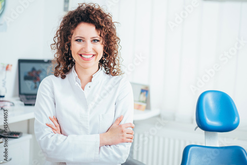 Portrait of female dentist. She standing at her office and she has beautiful smile.