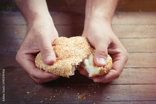 photo of male hand touching fresh bun with sesame on the wonderful brown wooden background