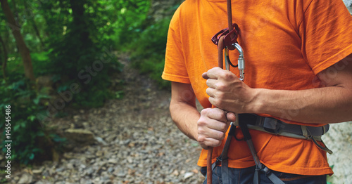 A man insures climber through a belay device. Tubular device on locking carabiner. hands and belay device close up