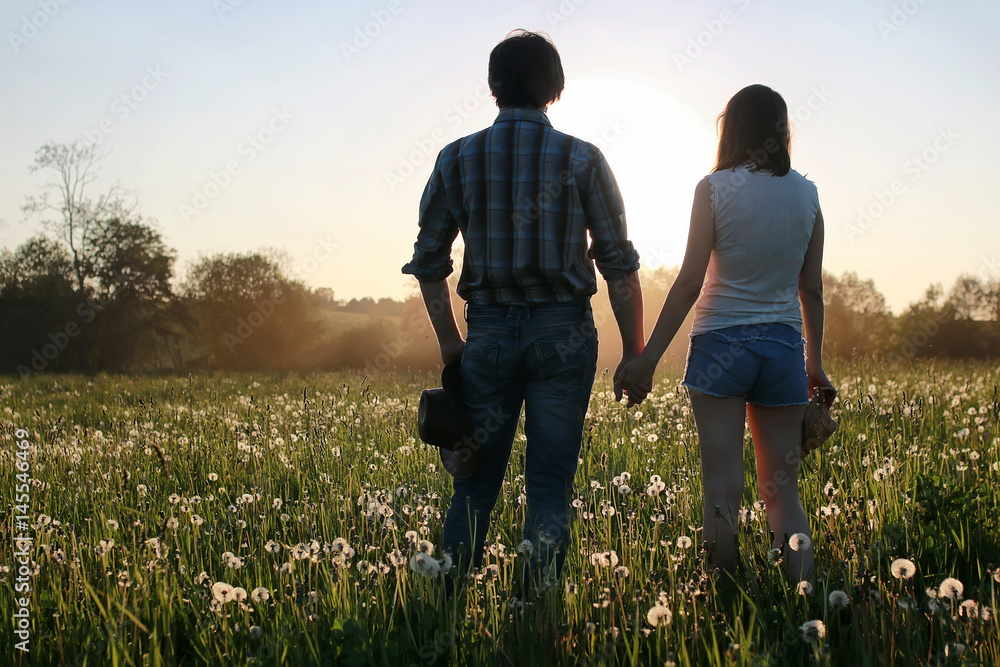 couple of young people walking in the sunset spring evening in a field
