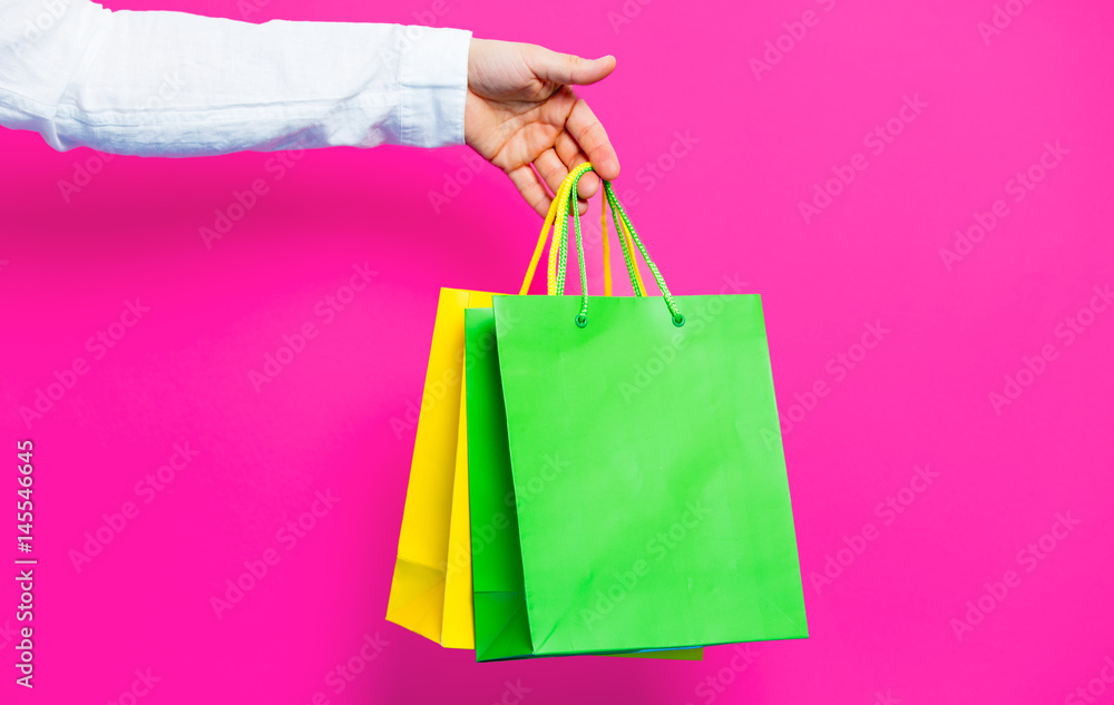 photo of female hand holding shopping bags on the wonderful pink studio background