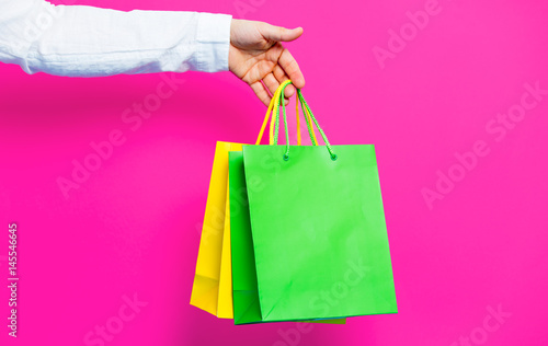 photo of female hand holding shopping bags on the wonderful pink studio background