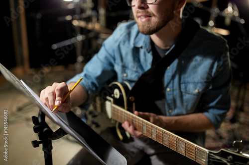 man with guitar writing to music book at studio