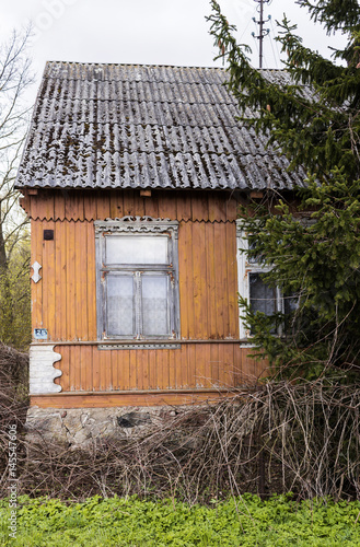 An abandoned wooden house with walls painted yellow-orange paint. Window with carved clypeus. Spring in the Region Podlasie, Poland.