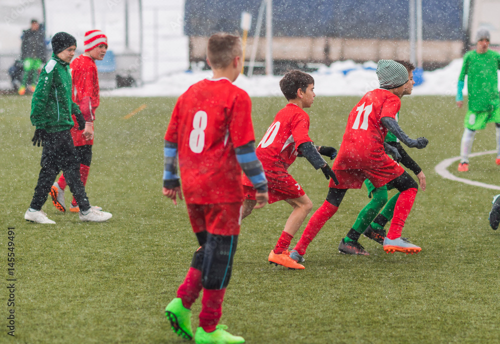 Obraz premium Kids soccer football tournament - children players match on soccer field during the snow falling