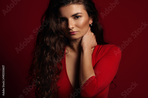model touches her neck and watches in camera, on red background