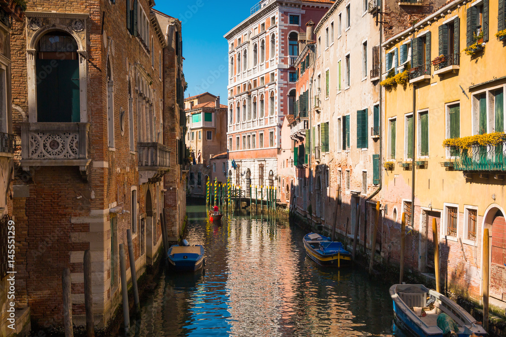 Narrow street with a canal, bridge, boats and tourists in Venice