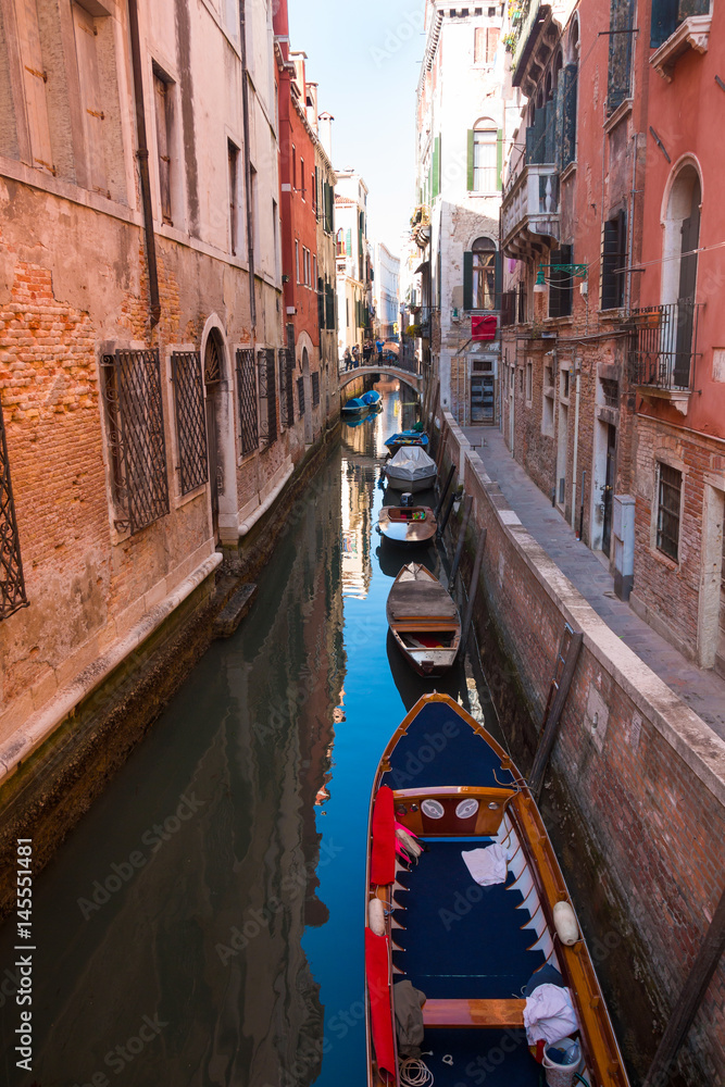 Narrow street with a canal, bridge, boats in Venice