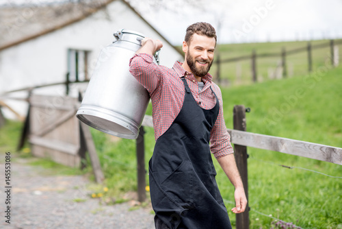 Schilderij op canvas Portrait of a handsome milkman in apron walking with milk container outdoors on