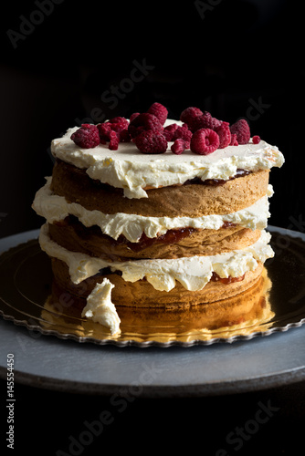 Delicious layered sponge cake with icing cream and raspberries