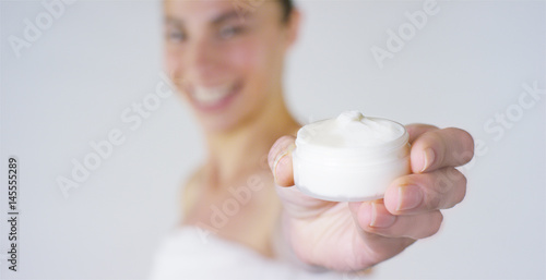 Fototapeta Naklejka Na Ścianę i Meble -  Portrait of a beautiful young girl smiling and looking at the camera, without makeup, holding cream, on a white background. Concept:natural beauty, youth, skin care, always young, love yourself.