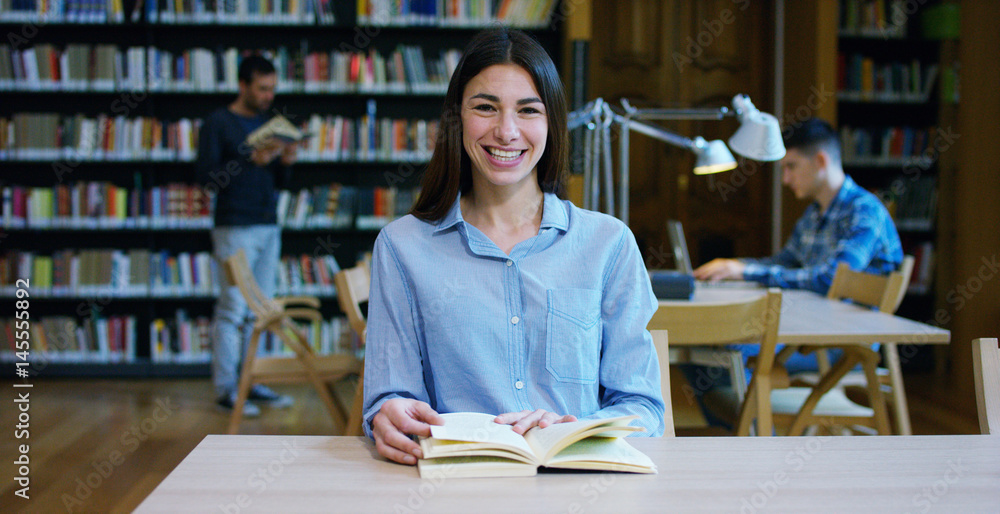 Portrait of a beautiful young woman smiling happy in a library holding books after doing a search and after studying. Concept: educational, portrait, library, and studious. Portrait of a beautiful young woman smiling happy in a library holding books after doing a search and after studying. Concept: educational, portrait, library, and studious.