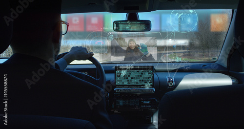 A businessman riding in a futuristic car and following a conference of economics and finance while driving. The call appears in augmented reality with projection of holograms