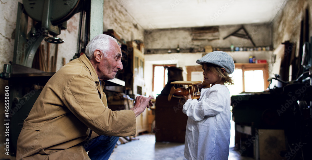 in an old carpentry shop a child and grandfather playing with a wooden airplane concept of tradition that continues over time	