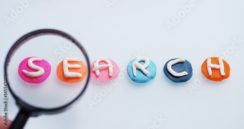 A magnifying glass hovers over the word "search" done in a creative and artistic as children. Concept of research, protected sites, creativity and color