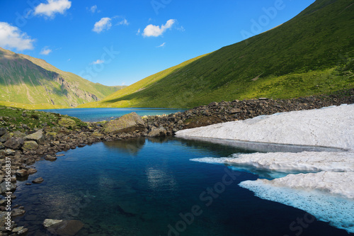 Mountain Lake in the mountains of Western Caucasus. Bright blue sky and white clouds.