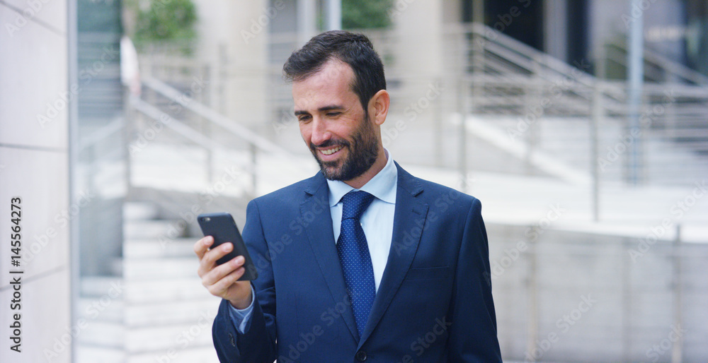 A businessman answering the phone, send messages and smiles for the beautiful job news and in the background you see a skyscraper. Concept: technology, telephony, business trips, business, wall street A businessman answering the phone, send messages and smiles for the beautiful job news and in the background you see a skyscraper. Concept: technology, telephony, business trips, business, wall street
