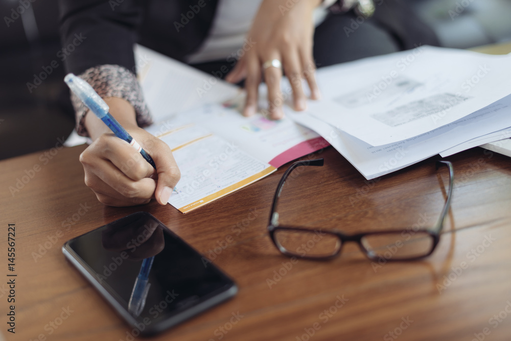 Asian female accountant or banker is busy working with laptop, smart phone and document in home office in selective focus. Concept : Busywork Asian female accountant or banker is busy working with laptop, smart phone and document in home office in selective focus. Concept : Busywork